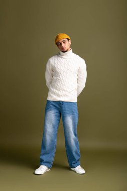 Şık genç adam kendine güvenerek duruyor, çekici bir varlıkla trend bir görünümü kucaklıyor..