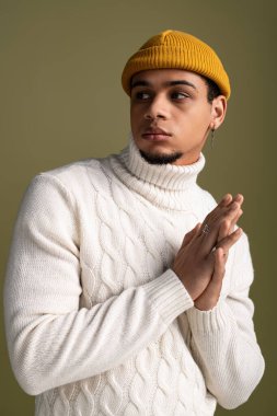 Genç adam zarif bir balıkçı yaka ve bereyle yumuşak bir arka plana karşı düşünceli bir şekilde poz veriyor..