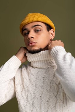 Yakışıklı genç adam rahat balıkçı yaka kazak ve parlak bereyle rahatça poz veriyor..