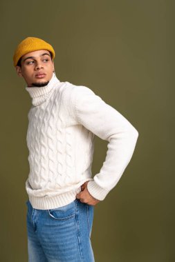 Genç adam şık bir tarz sergiliyor rahat bir süveter ve şapkayla, büyüleyici ve kendine güvenle.