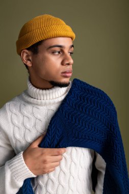 Kendine güveni tam bir genç adam, desenli bir süveter ve modaya uygun bir şapka takıyor, havalı bir tarzı ve cazibesi var..