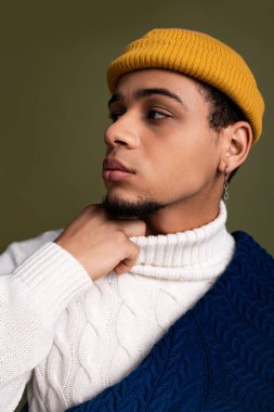 Genç adam şık bir kış elbisesi içinde cesur sarı bir bereyle düşünceli bir şekilde poz veriyor..