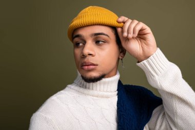 Şık giyinmiş yakışıklı bir genç adam sağlam bir arka plana karşı düşünceli bir şekilde poz verir.