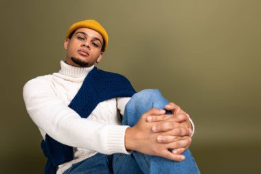 Rahat bir ortamda, genç bir adam rahat bir şekilde otururken şık görünümünü sergiliyor..