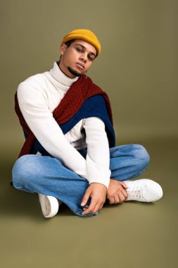 Moda kıyafetli genç adam arka planda otururken eşsiz bir stil sergiliyor..