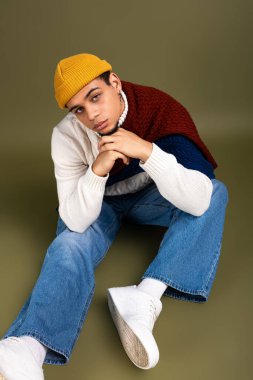 Yakışıklı genç bir adam kendine güvenerek oturur şık giyinir, modern moda eğilimlerini somutlaştırır..