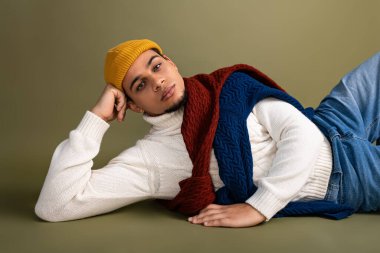 Genç adam şık bir arka planda rahatlıyor, şık kıyafetlerini ve kendine güvenen tavırlarını sergiliyor..