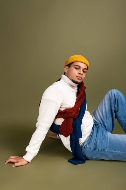 Şık giyinmiş genç bir adam sağlam bir arka plana karşı gevşiyor, kendine güveni ve tarzı var..