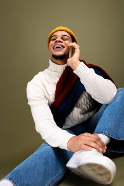 Genç adam telefonda konuşurken neşeli bir şekilde gülüyor. Şık, rahat giysiler içinde..