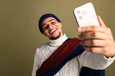 Yakışıklı genç adam sıcak kış modasına uygun giyinmiş bir selfie çekerken ışıl ışıl gülümsüyor..