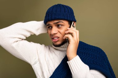 Rahat bir süveter giyen genç bir adam telefonda konuşuyor, endişeli görünüyor..