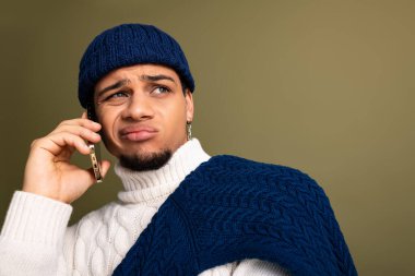 Yakışıklı genç adam telefonda konuşurken şık bir süveter ve şapka giyiyor..
