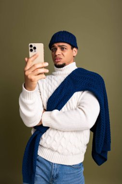 Modayı takip eden genç bir adam şık kıyafetler giyerken elinde akıllı bir telefon tutuyor..