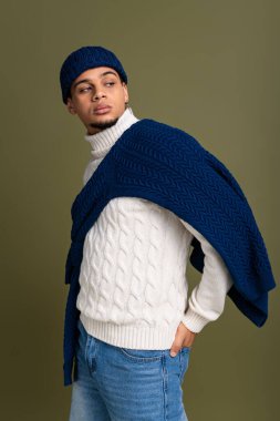 Şık giyimli bir adam, rahat bir süveter ve parlak renklerde bir şapka giyer..