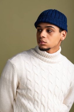 Genç bir adam zarif bir süveter ve örgü şapkayla modern moda anlayışını sergiliyor..