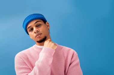 Yakışıklı genç adam modaya uygun pembe süveter ve mavi şapkayla kendine güvenerek poz veriyor..