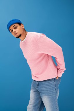 Pembe süveter ve kot pantolonlu genç adam canlı bir arkaplanda poz veriyor..
