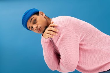 Pembe kazaklı ve mavi bereli genç bir adam havalı moda titreşimleri yayıyor..