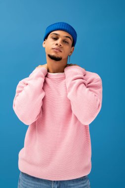 Yakışıklı genç adam dikkat çekici bir portre ortamında moda pembe bir kazak ve mavi şapka giyiyor..