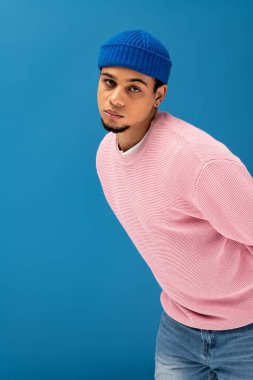 Pembe kazaklı ve mavi şapkalı yakışıklı genç adam yaratıcı bir ortama özgüvenle poz veriyor..