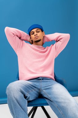 Modaya uygun genç bir adam şık bir pozisyonda rahat ve modaya uygun pembe bir kazak ve mavi bir bere giyiyor..