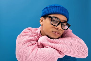 Kendine güvenen genç bir adam rahat bir süveter ve bereyle poz verir, büyüleyici ve modaya uygun..