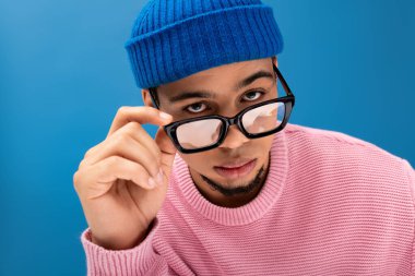 Kendine güveni tam genç bir adam, gözlüğünü şık pembe bir kazak ve mavi bir bere giyerken ayarlıyor..