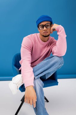 Yakışıklı genç adam canlı mavi arkaplana karşı kendine güvenen bir şekilde poz veriyor..