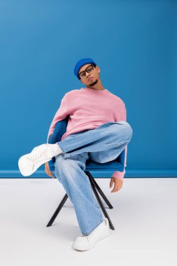 Şık giyinen genç adam yaratıcı bir poz vererek, cesur renkleri ve modern modayı ön plana çıkarıyor..