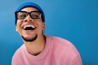 Şık bir genç adam mavi arka planda ışıl ışıl gülümser.