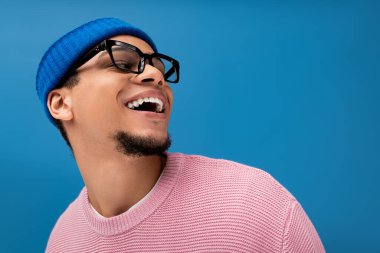 Gözlüklü şık bir genç adam ve bir bere renkli bir ortamda ışıl ışıl gülümsüyor..