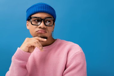 Moda kıyafetli yakışıklı genç adam, parlak mavi bir arkaplana karşı güven yayıyor..