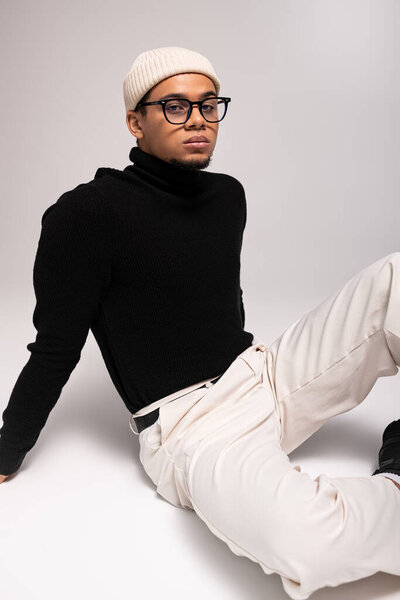 Young man in a black turtleneck and white pants poses stylishly, exuding confidence and flair.