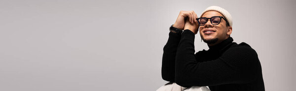 A handsome young man dressed in fashionable attire sits casually, exuding charm and confidence.