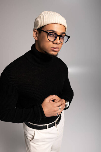 Young man confidently posing in trendy attire against a simple backdrop.