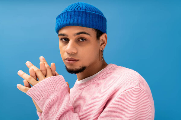 Молодой человек демонстрирует чувство моды в модном наряде и уникальной шляпе на смелом фоне.