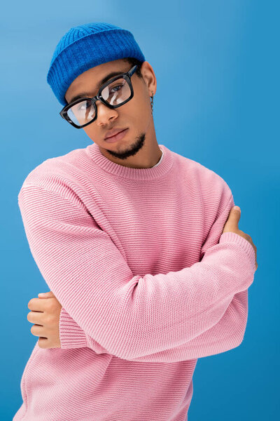Красивый молодой человек уверенно позирует в модном розовом свитере и голубой шапочке.