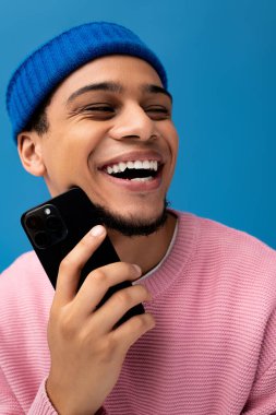 Moda kıyafetli yakışıklı genç adam akıllı telefonunu tutarken neşeli bir anı paylaşıyor..