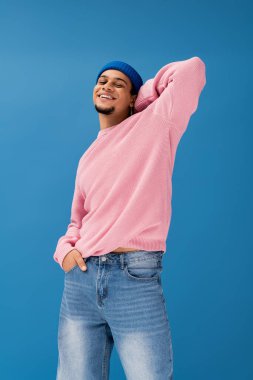 Pembe süveter ve günlük mavi kot pantolon giyen genç bir adam neşe saçıyor..