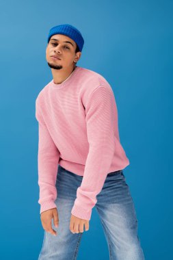 Genç adam, parlak, mavi bir zemine karşı, kendine güvenen modaya uygun bir şekilde poz veriyor..