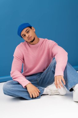 Yakışıklı genç adam, canlı mavi bir arkaplan karşısında gündelik tarzda modern moda sergiliyor..