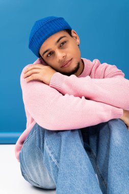 Tarz sahibi genç bir adam canlı bir arka planda güvenle oturur..