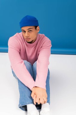 Şık bir genç adam renkli bir arkaplan karşısında kendine güvenerek poz verir..