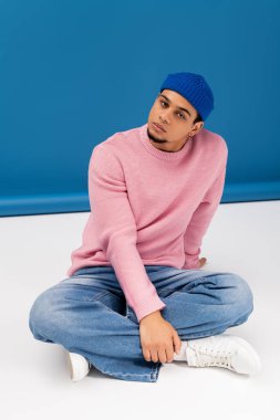 Şık bir genç adam, sıradan bir şekilde yerde oturur ve şık bir kıyafete güvenir..