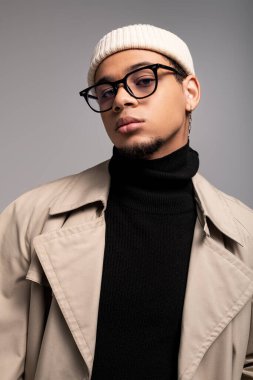 Şık bir genç adam kendine güvenerek poz veriyor. Moda kıyafetlerini benzersiz bir stüdyoda ön plana çıkarıyor..