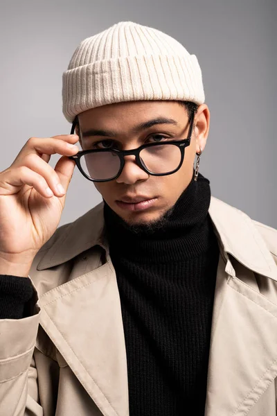 Şık giyinmiş özgüvenli genç adam gözlüklerini ayarlarken düşünceli bir şekilde poz veriyor..
