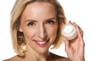 Gülümseyen sarışın kadın elinde bir krema kavanozu tutuyor, sağlıklı cildini yükseltiyor ve güzel görünüyor..