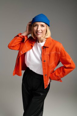 Şık sarışın bir kadın mavi bereli ve turuncu ceketli poz veriyor..