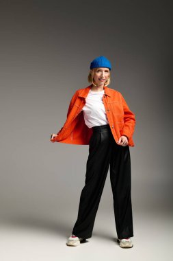 Şık, sarışın bir kadın stüdyoda turuncu ceketini ve mavi beresini modelliyor..