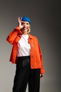 Zarif sarışın bir kadın turuncu ceketi ve mavi beresi ile neşe içinde gülümsüyor..